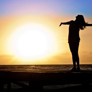 Woman with arms open on boardwalk at sunset